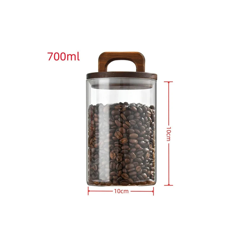 Glass coffee bean canister with wooden lid styled in a calm neutral kitchen with coffee beans and ceramic cup