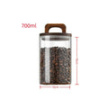 Glass coffee bean canister with wooden lid styled in a calm neutral kitchen with coffee beans and ceramic cup