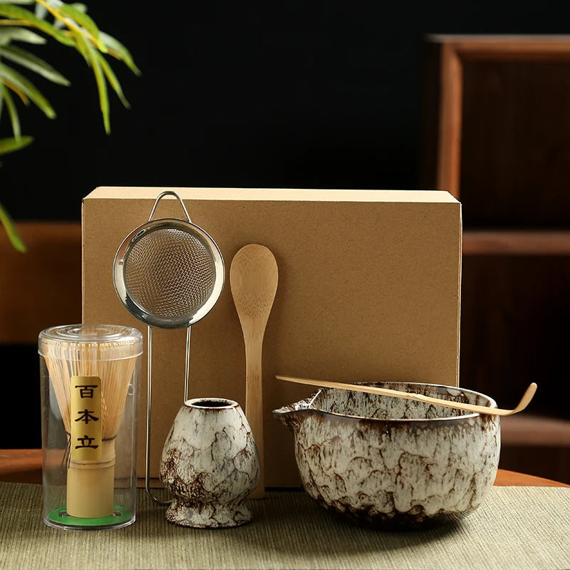 Japanese matcha tea set with ceramic bowl, bamboo whisk, whisk holder, tea strainer, and wooden scoop arranged in a calm neutral kitchen setting